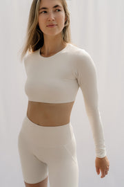 Woman wearing a white long-sleeve crop top and high-waisted leggings against a plain background
