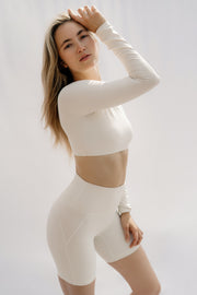Woman wearing a white long-sleeve crop top and high-waisted leggings against a light background