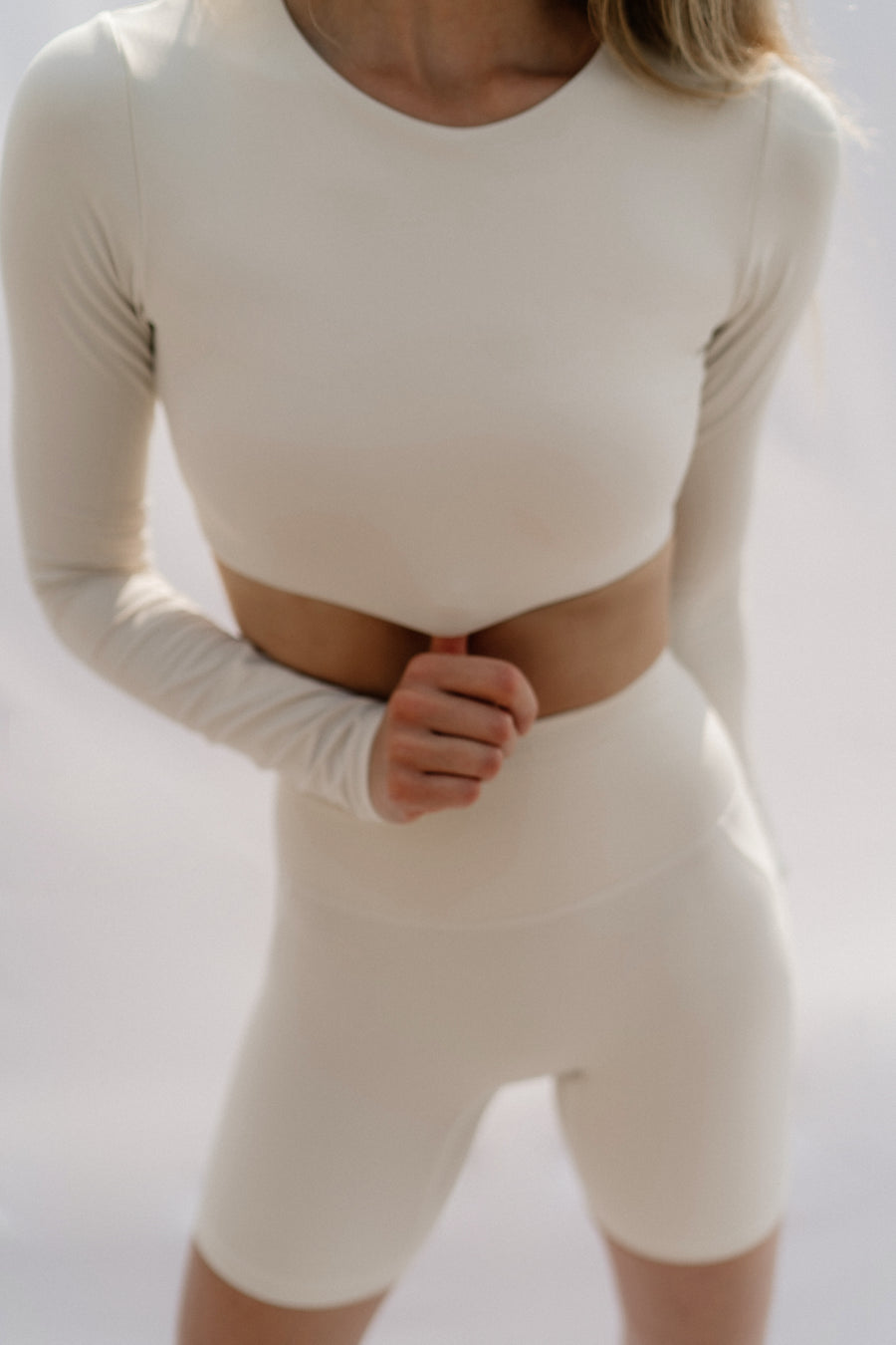 Woman wearing a white long-sleeve top and shorts set on a light background