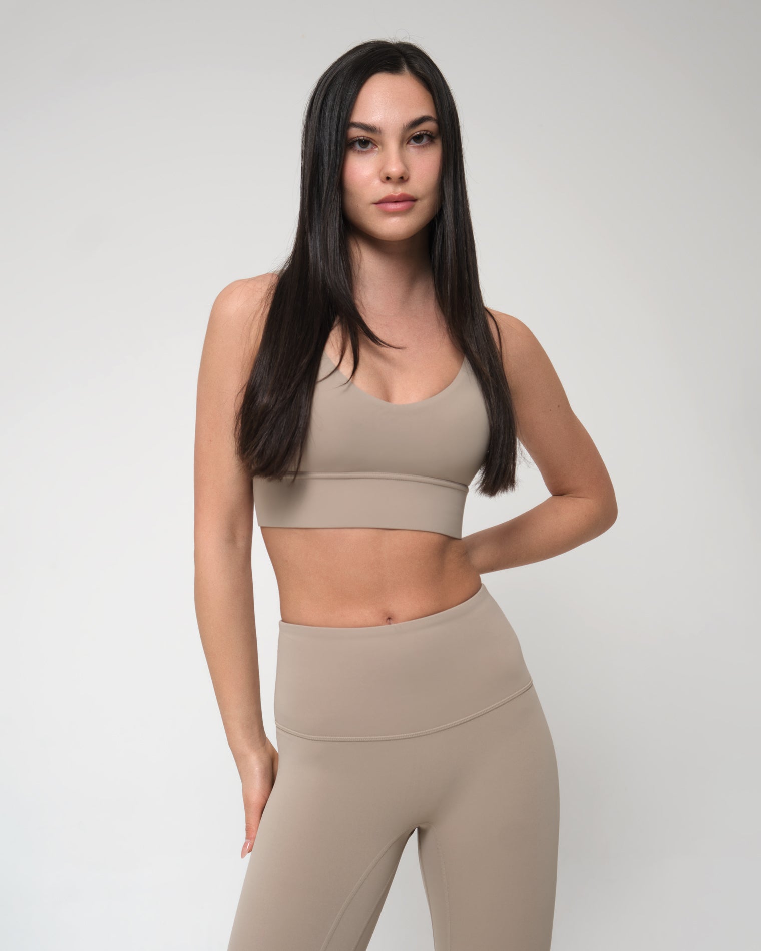 Woman wearing a beige sports bra and leggings on a plain background