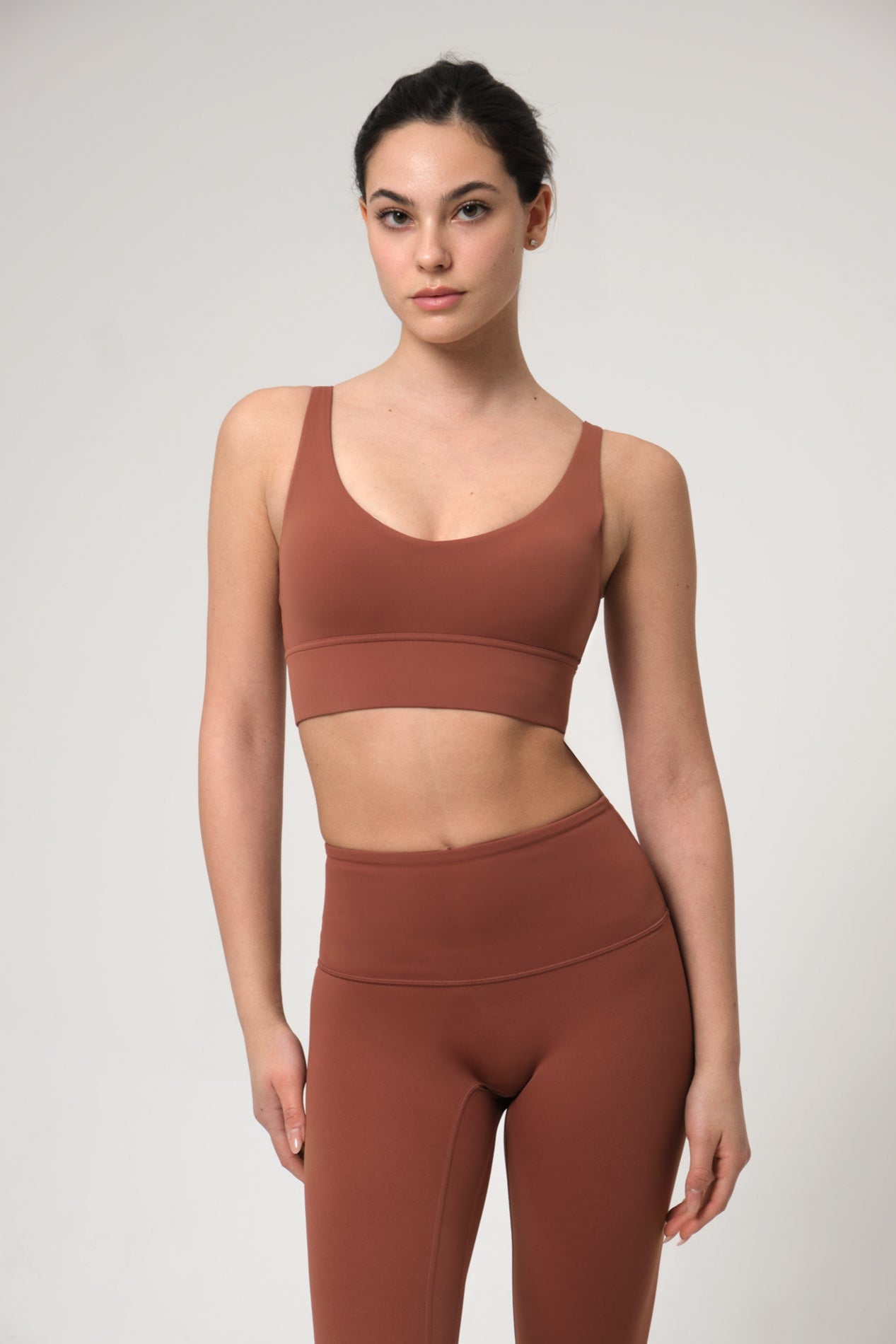 Woman wearing a brown sports bra and leggings set on a light gray background