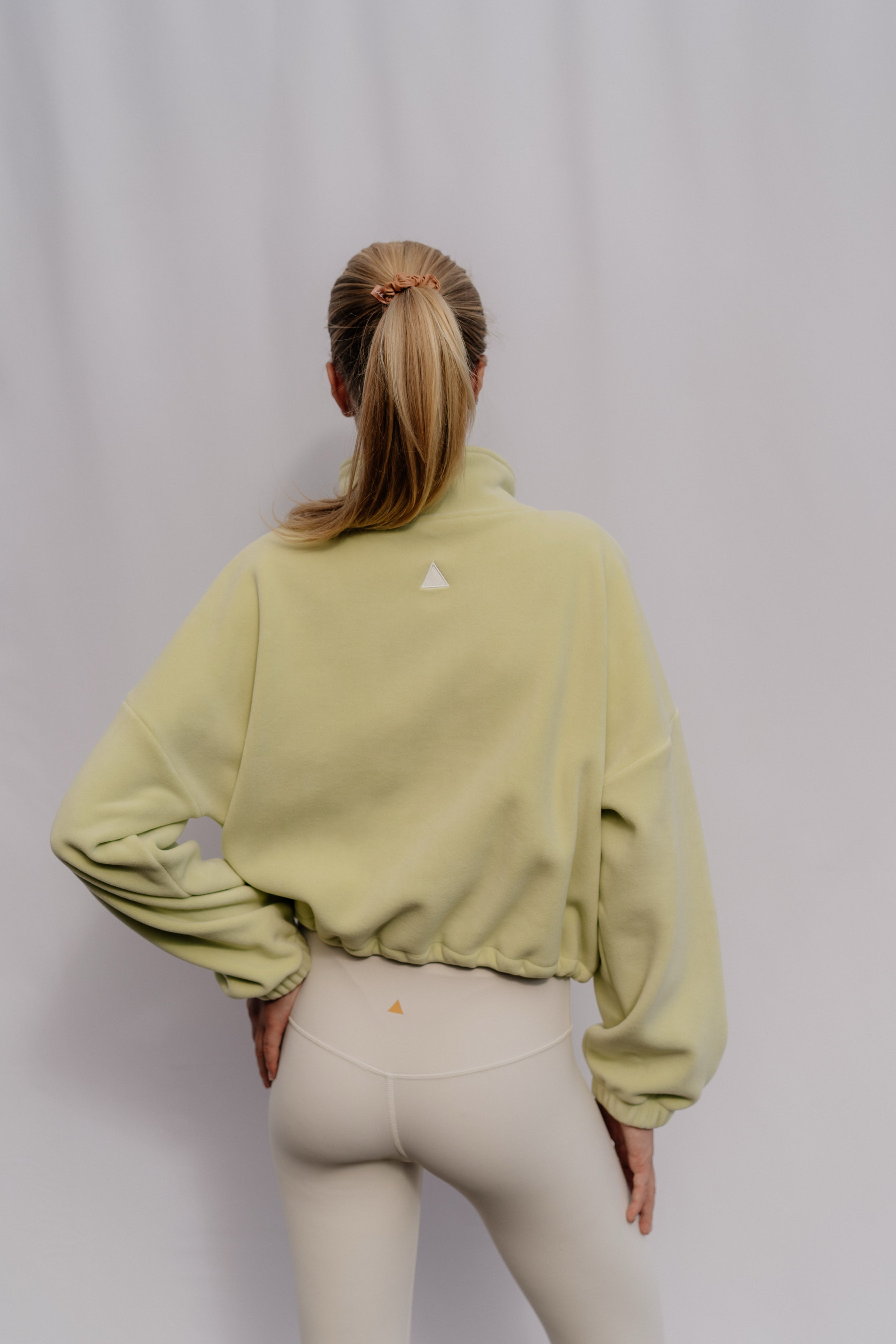 Person wearing a light green sweatshirt with a small logo on the back against a plain background