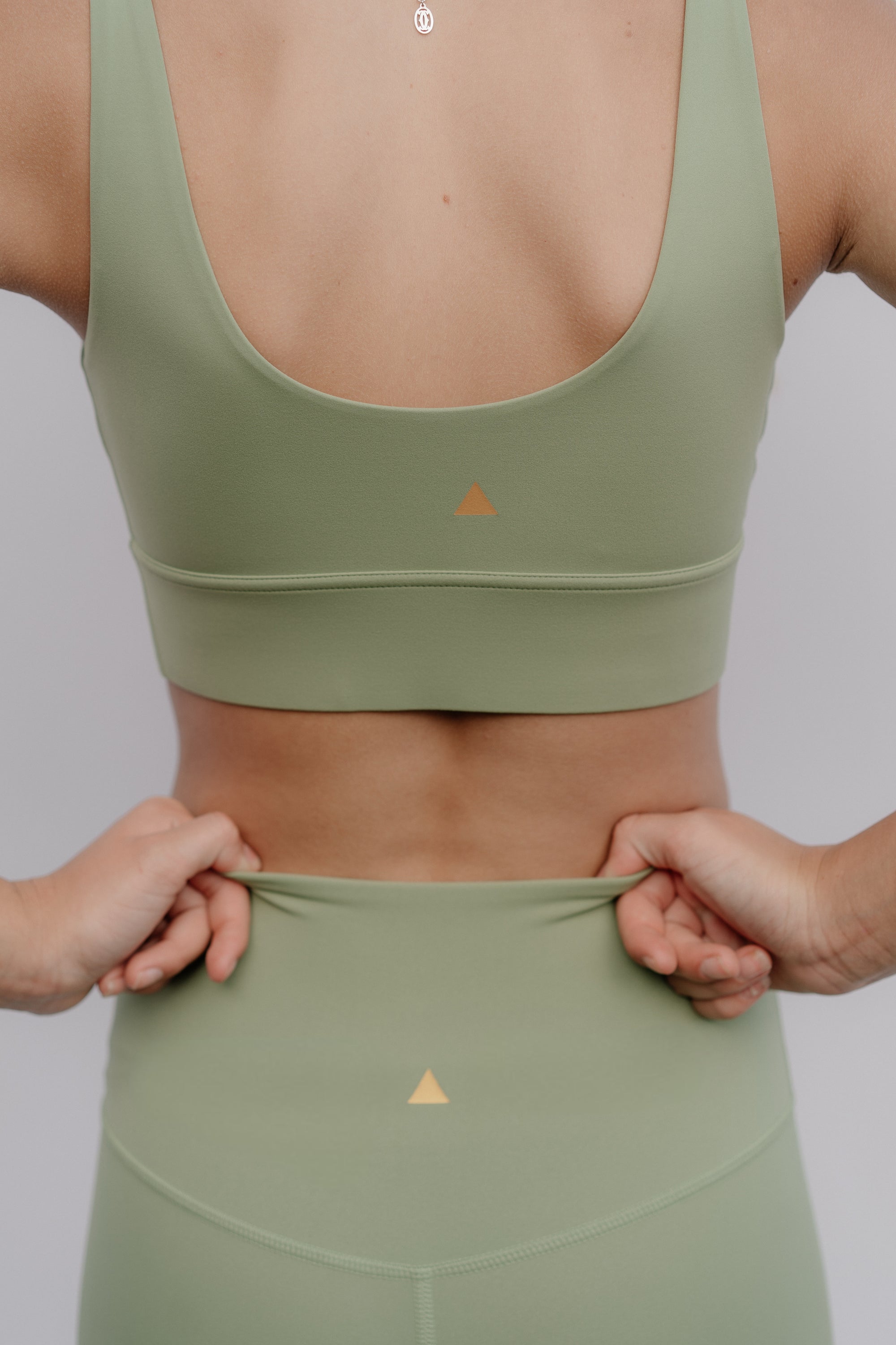 Person wearing a green sports bra and leggings with a triangle logo on a plain background