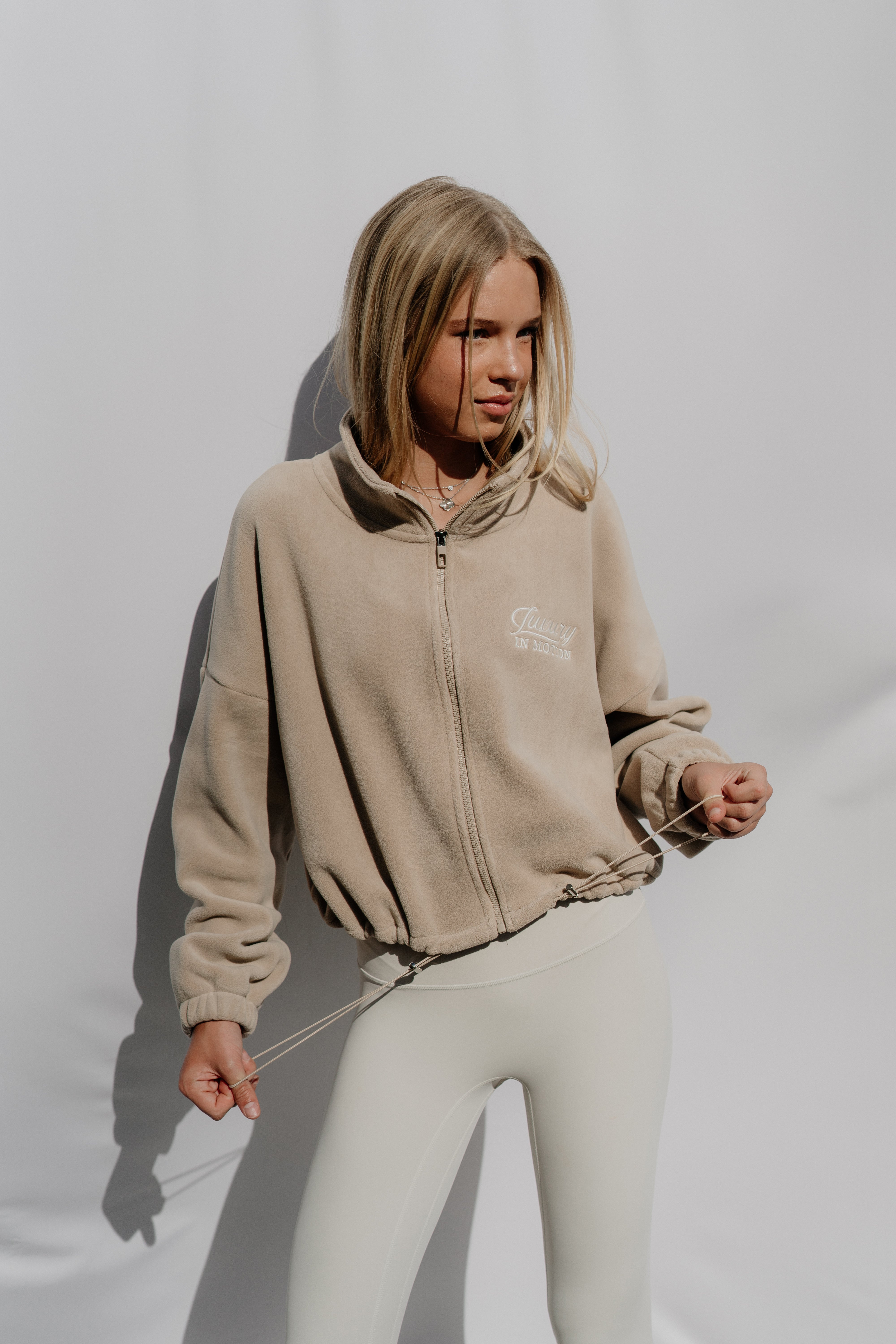 Woman wearing a beige jacket and white pants against a plain background