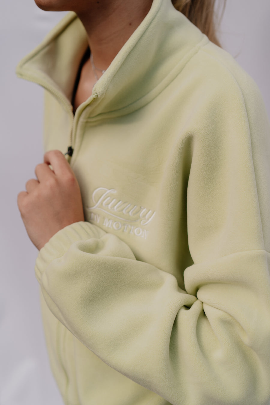 Light green fleece pullover with 'Luxury in Motion' branding on a plain background