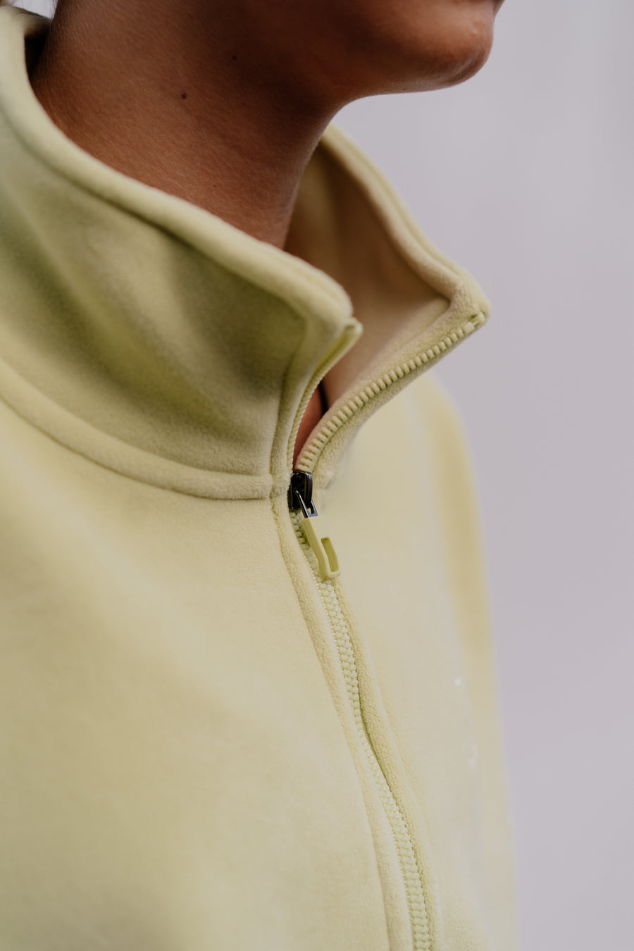 Close-up of a person wearing a light green fleece jacket with a zipper.
