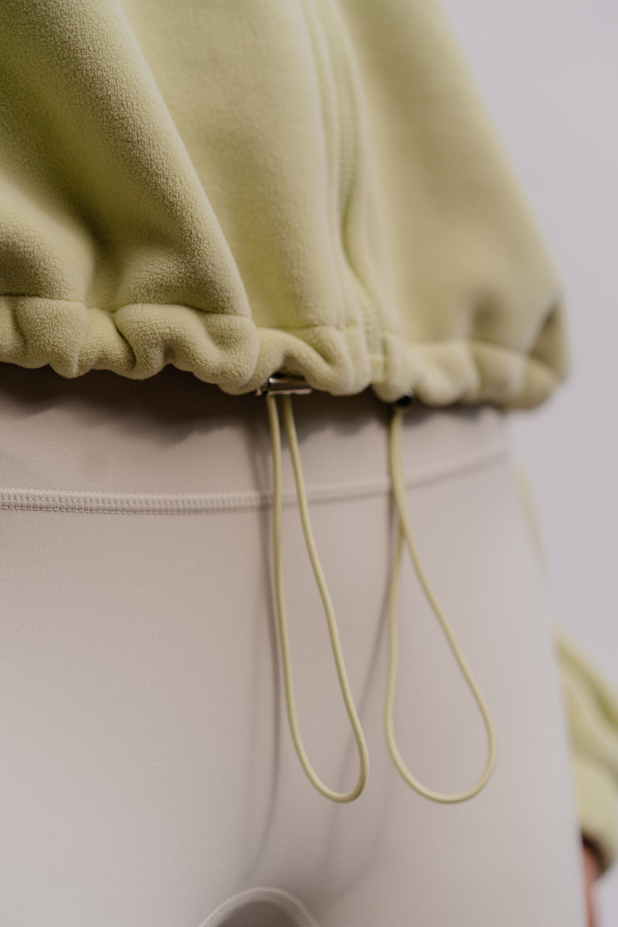 Close-up of a person wearing a light green cropped hoodie and beige pants.