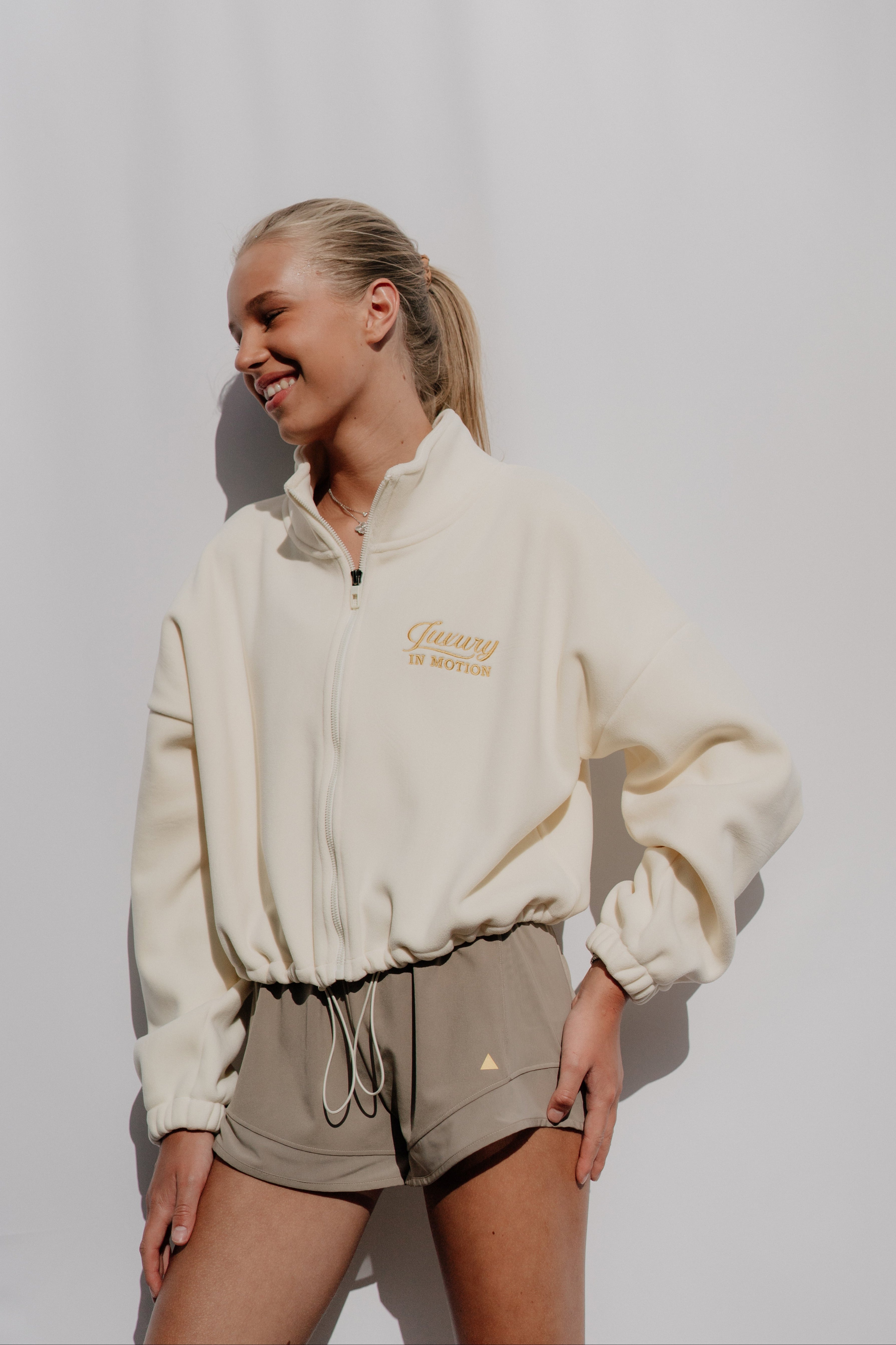Woman wearing a cream-colored jacket with a logo on a white background
