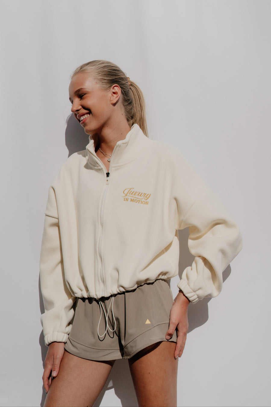 Woman wearing a cream-colored jacket with a logo on a white background