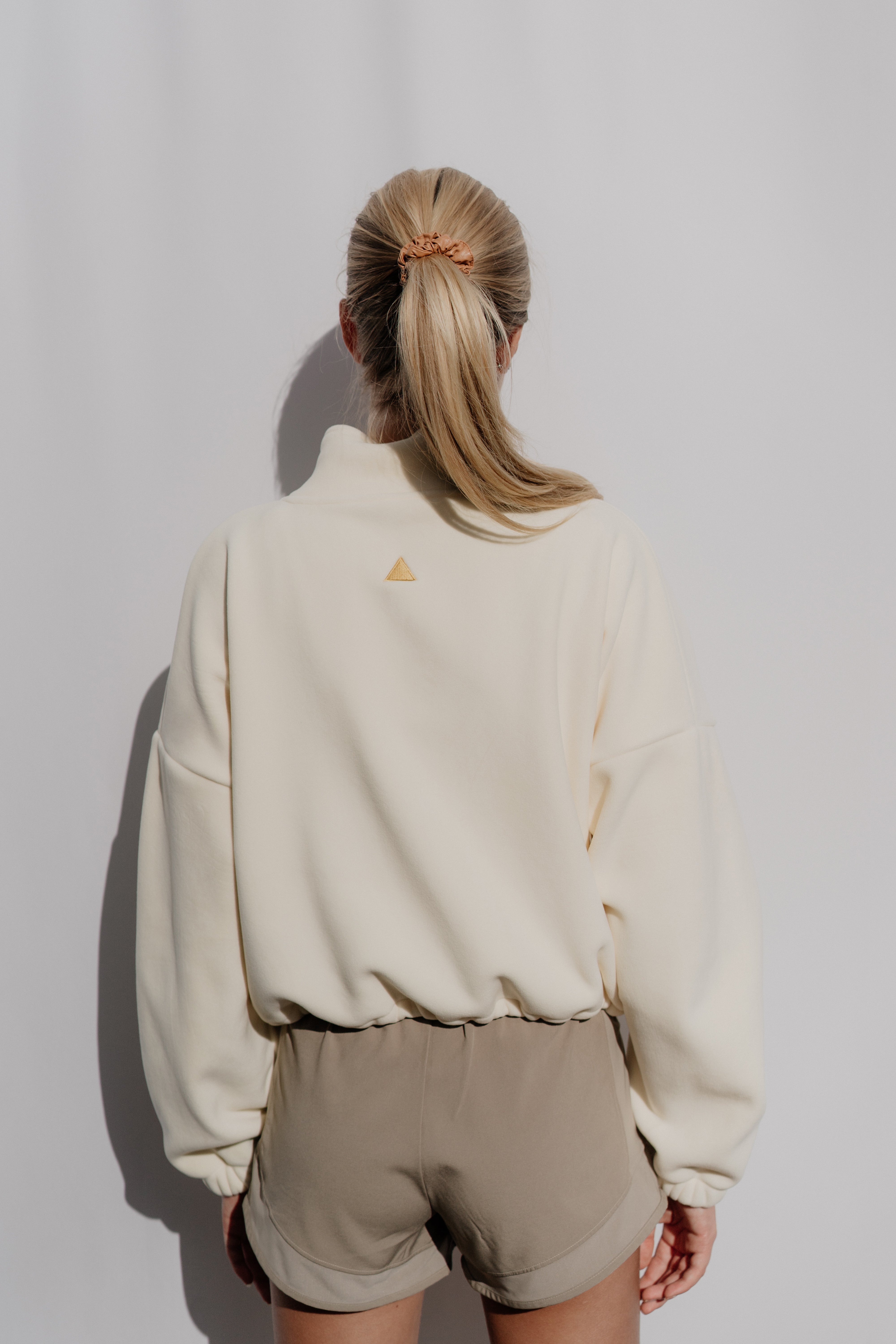 Person wearing a beige sweatshirt and shorts against a plain background