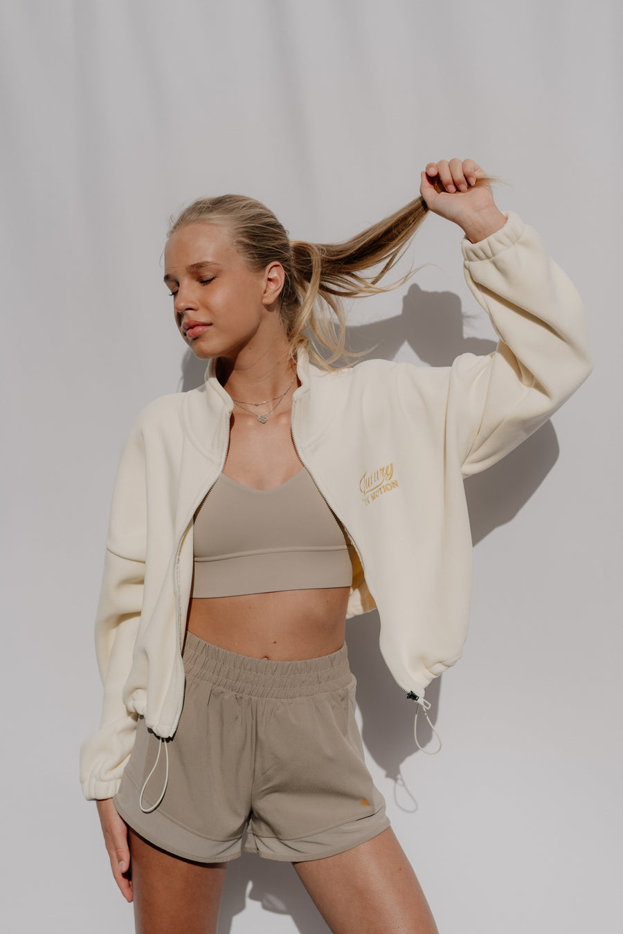 Woman in beige athletic outfit with jacket against a plain background