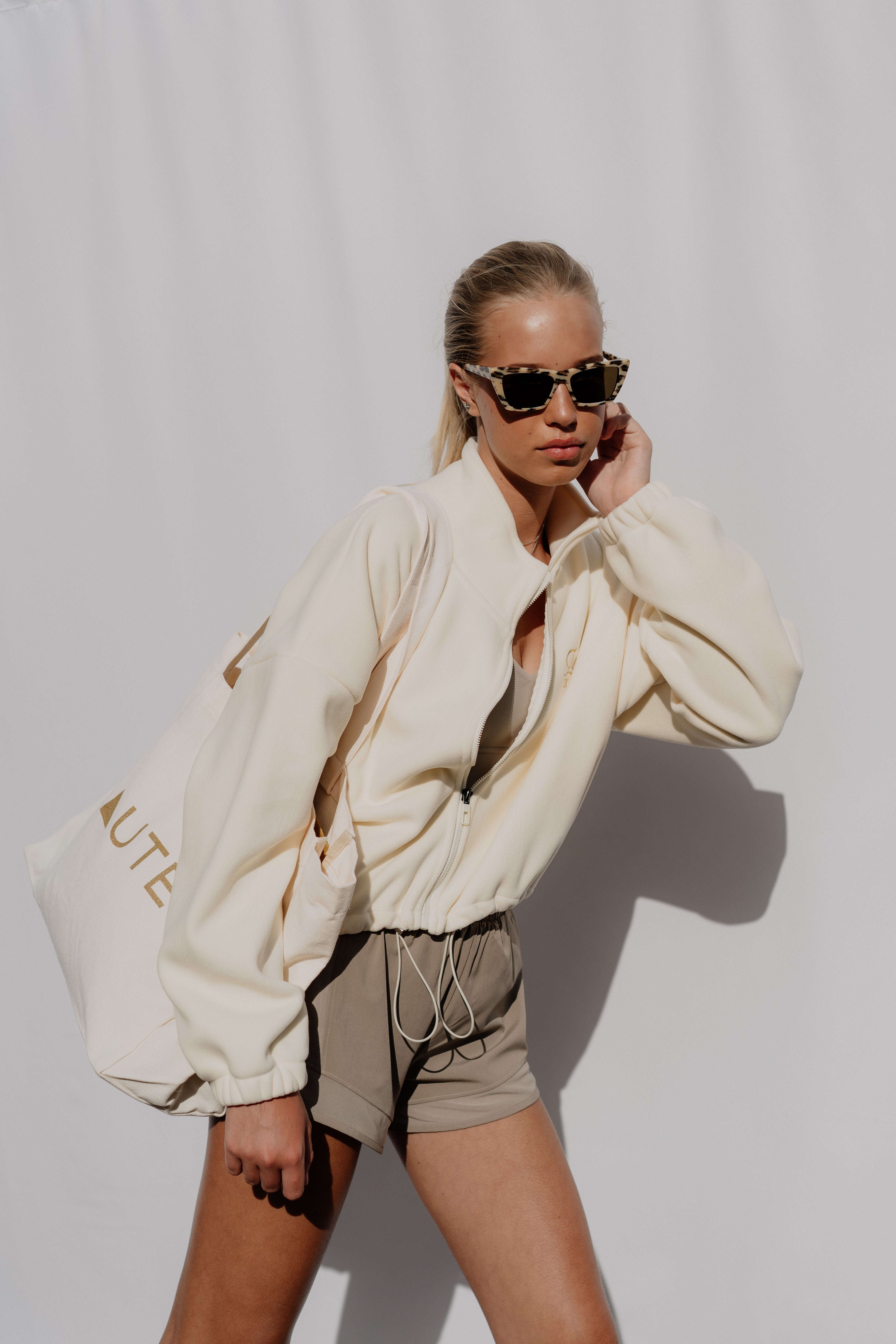 Woman wearing a beige oversized jacket and shorts against a white background