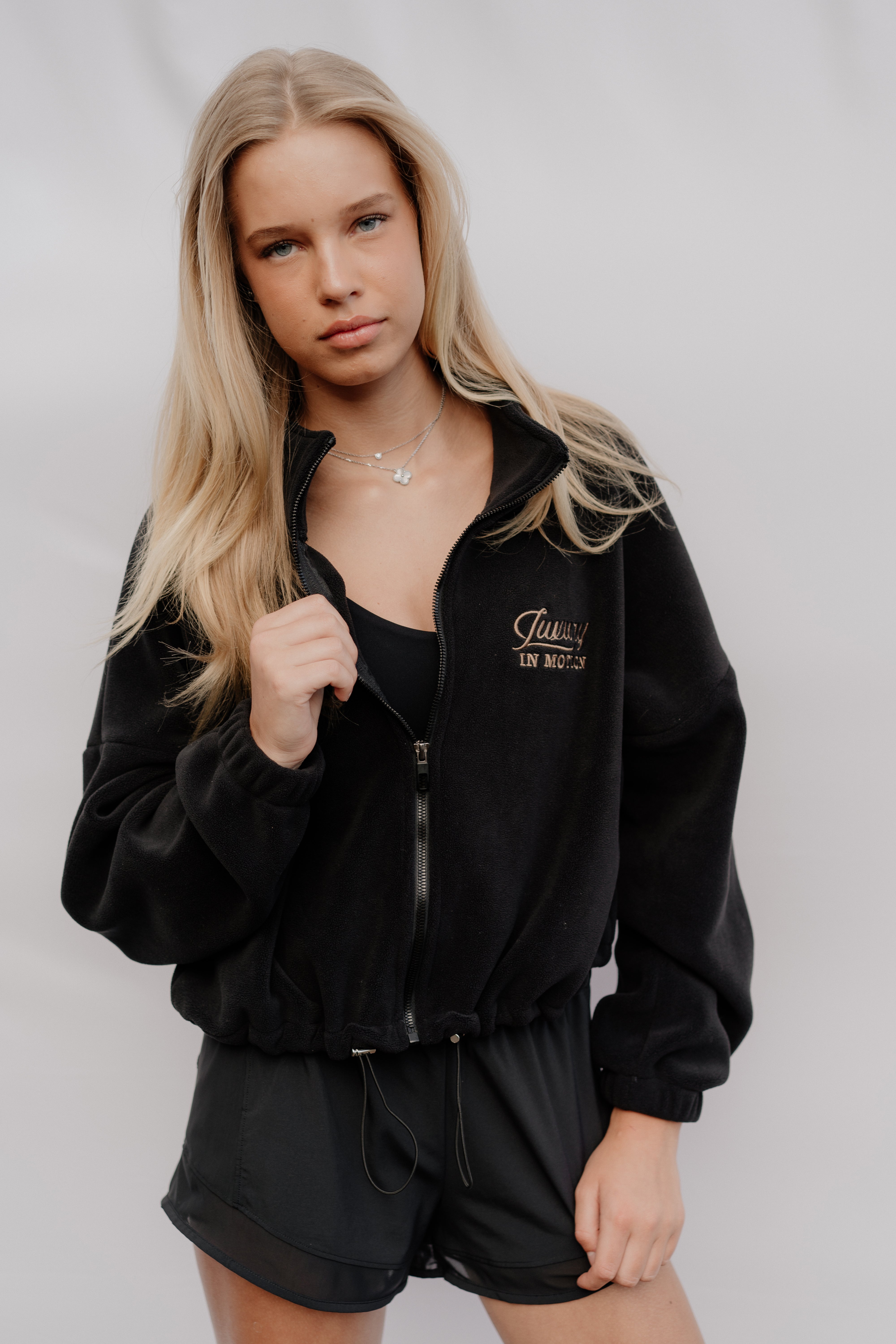 Person wearing a black tracksuit with a brand logo on a plain background