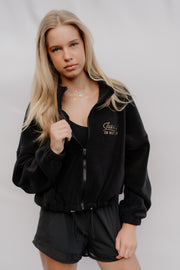Person wearing a black tracksuit with a brand logo on a plain background