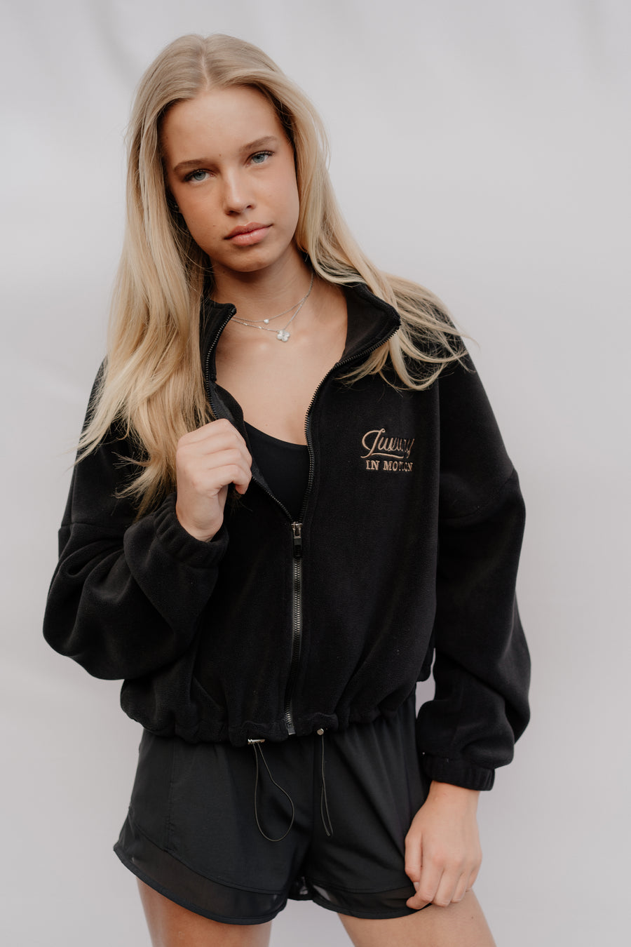 Person wearing a black tracksuit with a brand logo on a plain background