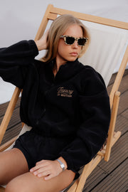 Woman wearing a black sweatshirt with 'Luxury in motion' text, sitting on a wooden deck chair.