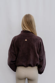 Woman wearing a brown jacket with a triangle logo on a plain background