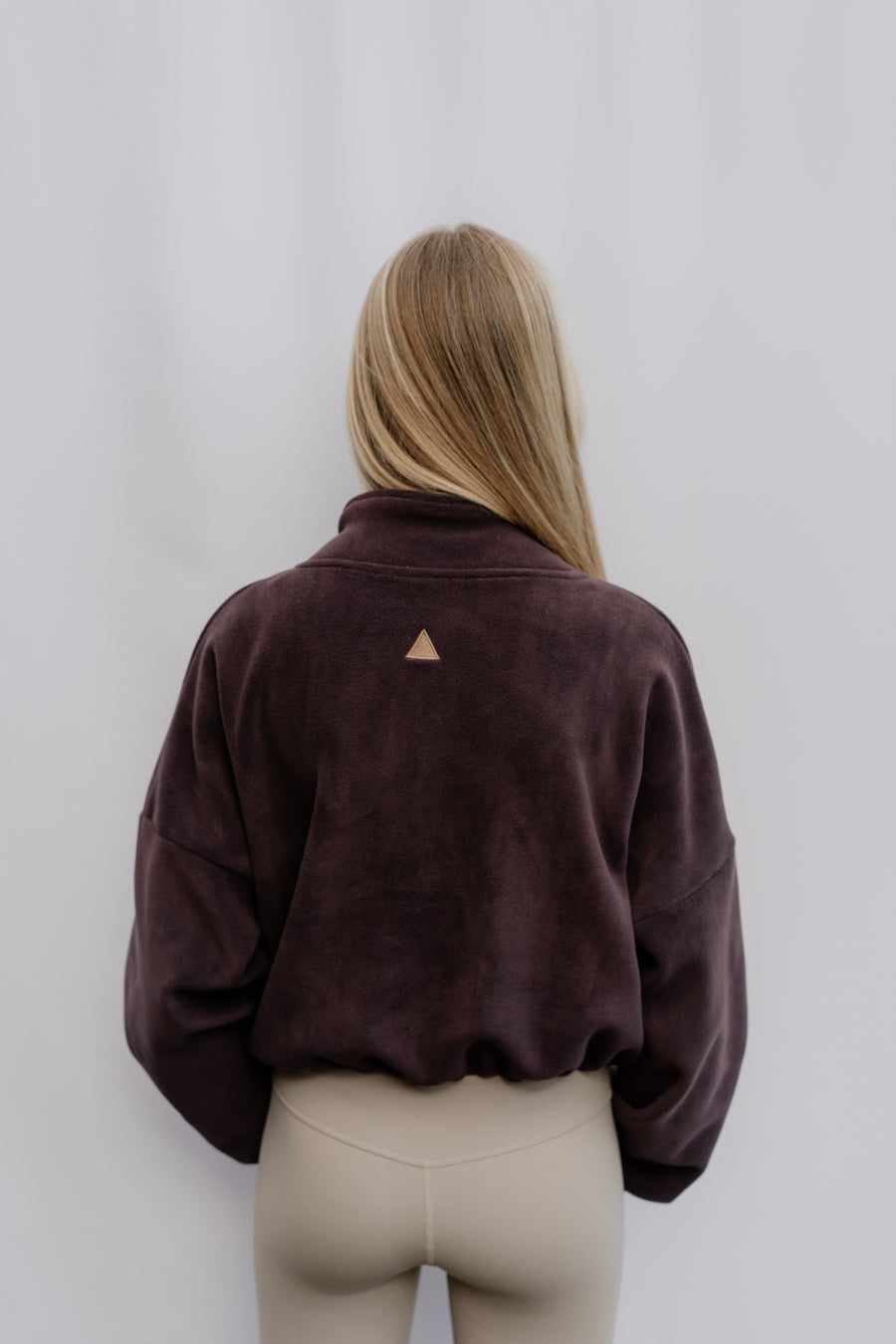 Woman wearing a brown jacket with a triangle logo on a plain background