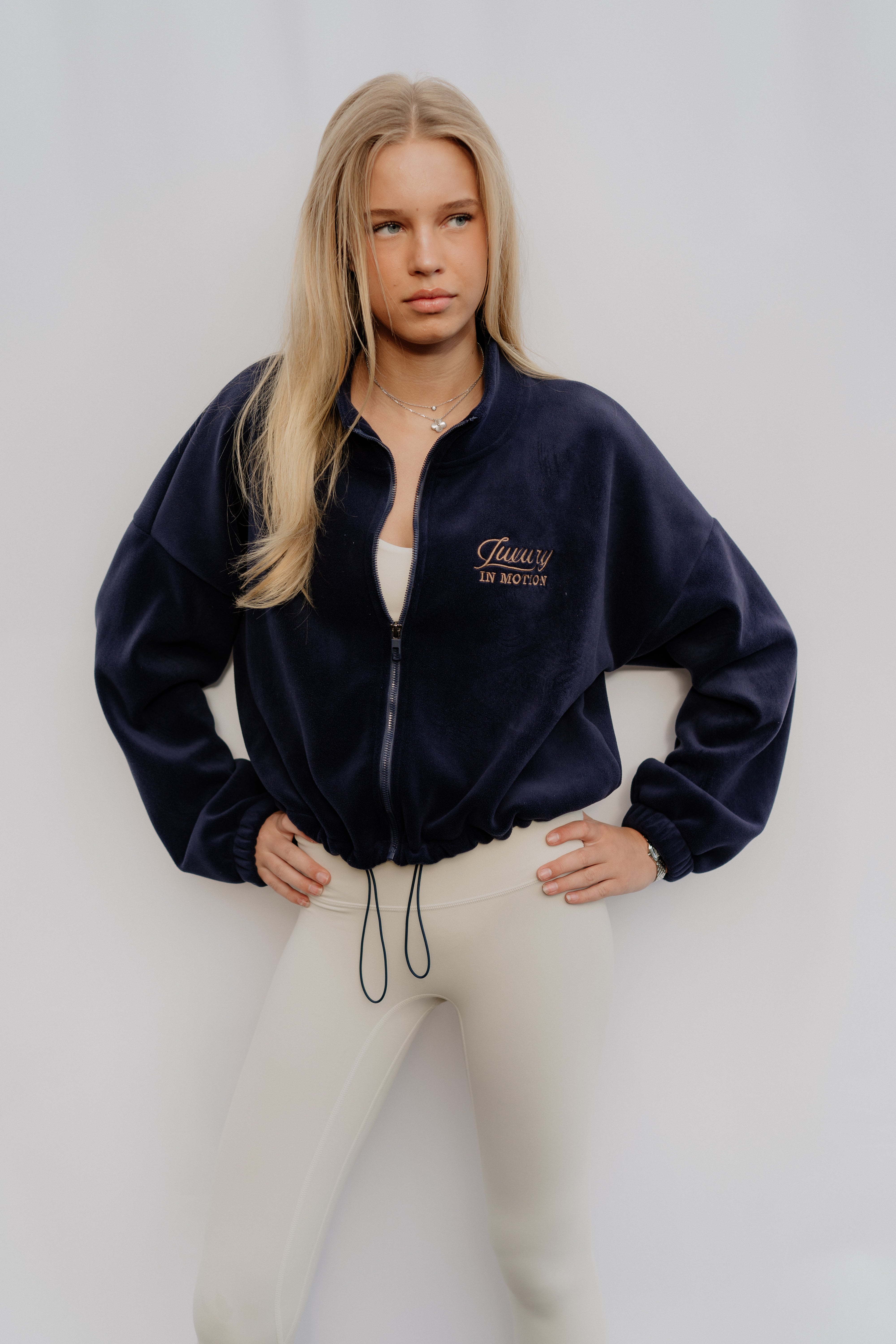 Woman wearing a navy blue jacket with a brand logo on a white background