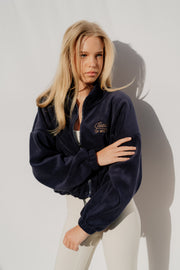 Woman wearing a navy blue jacket with a logo on a white background