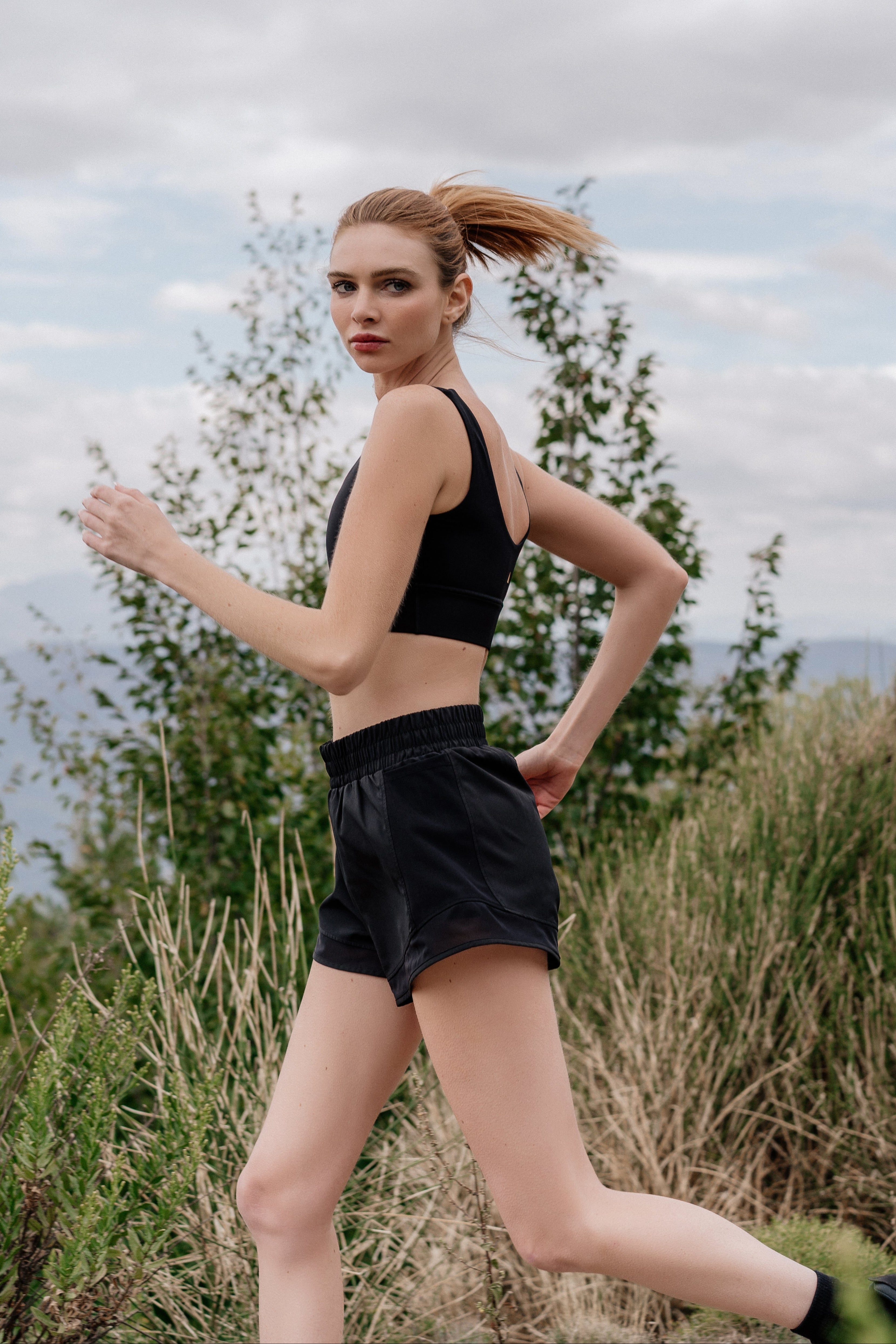 Woman in athletic wear running outdoors with trees and sky in the background