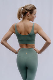 Woman wearing a green sports bra and leggings set on a plain background