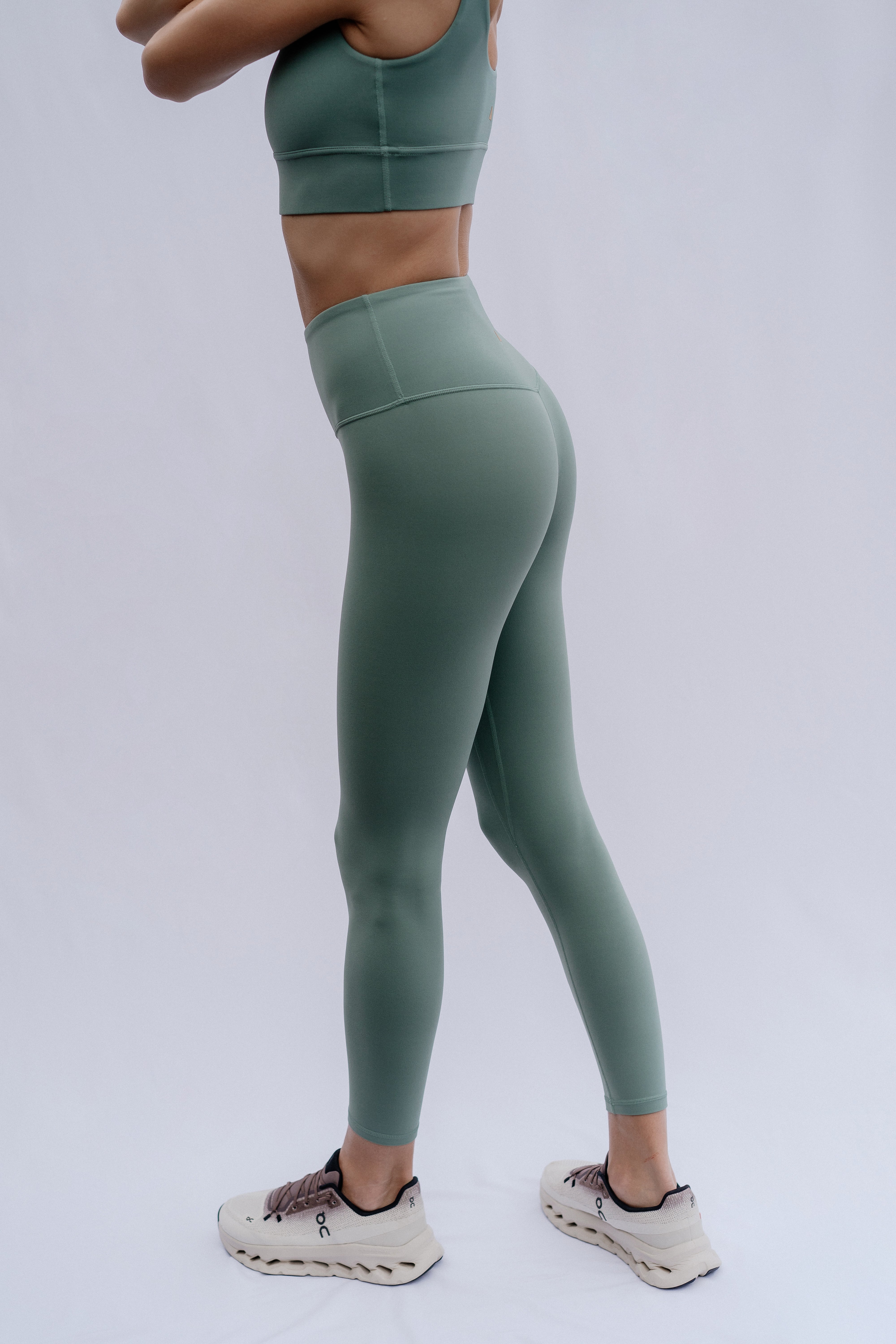Woman wearing green athletic leggings and sports bra on a plain background