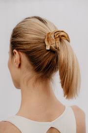 Woman with a ponytail held by a scrunchie against a plain background