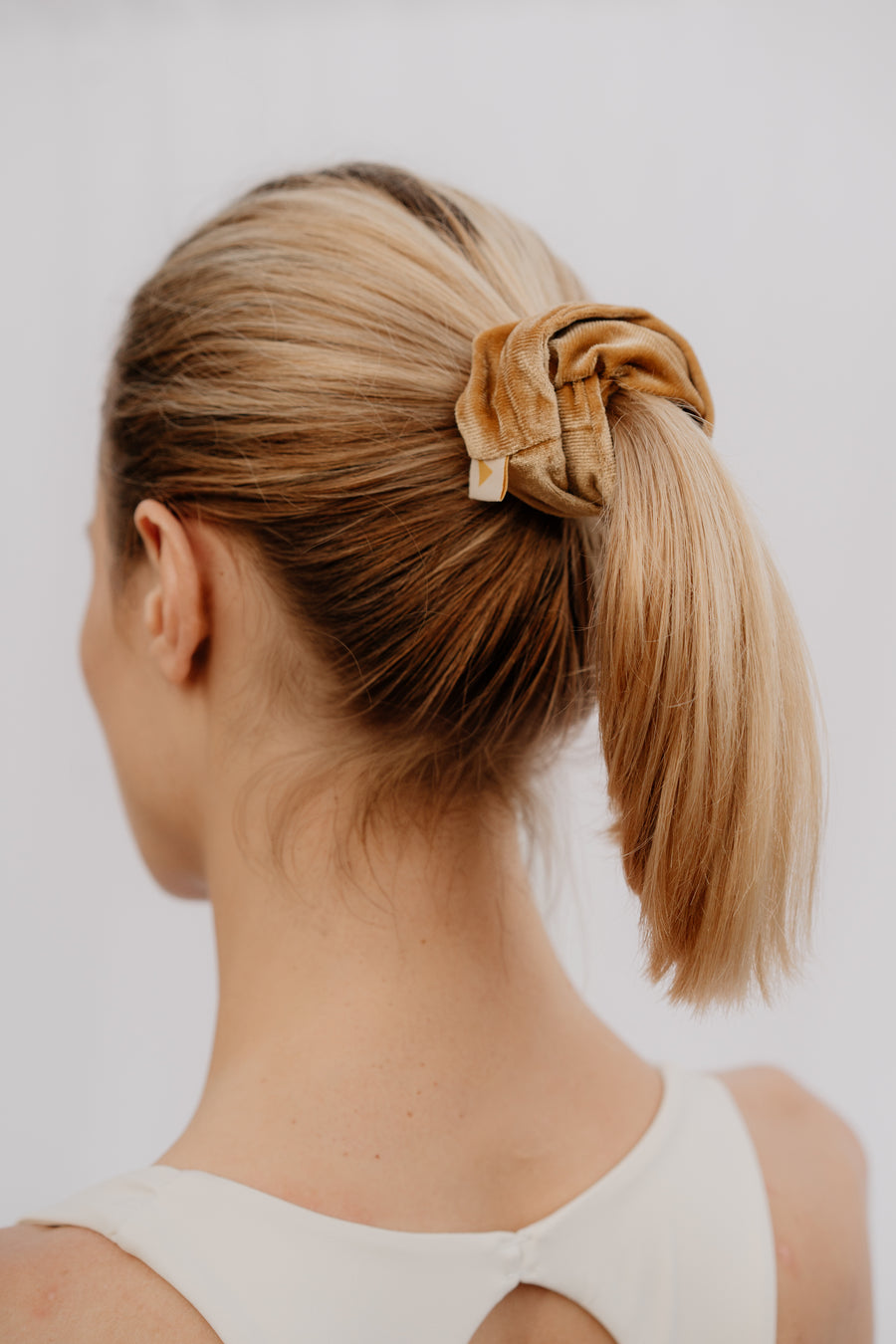 Woman with a ponytail held by a scrunchie against a plain background