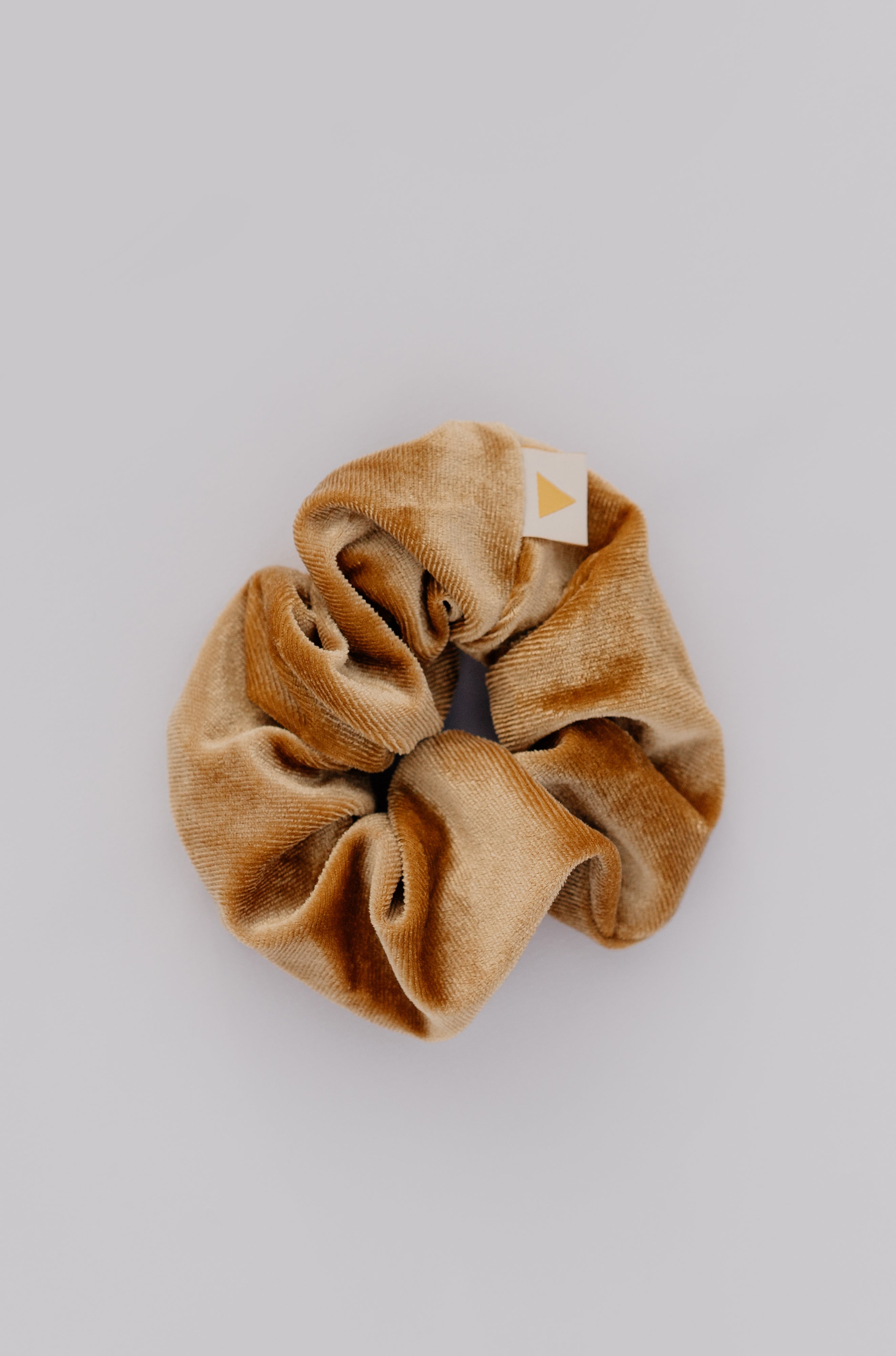 Golden scrunchie with a brand tag on a light gray background