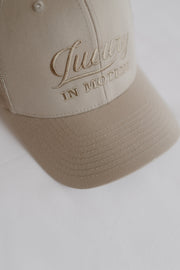 Beige cap with 'Luxury in Motion' embroidery on a white background