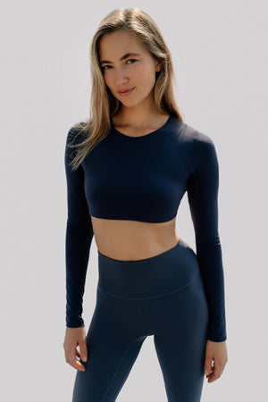 Woman wearing a navy long-sleeve athletic top and leggings on a light gray background