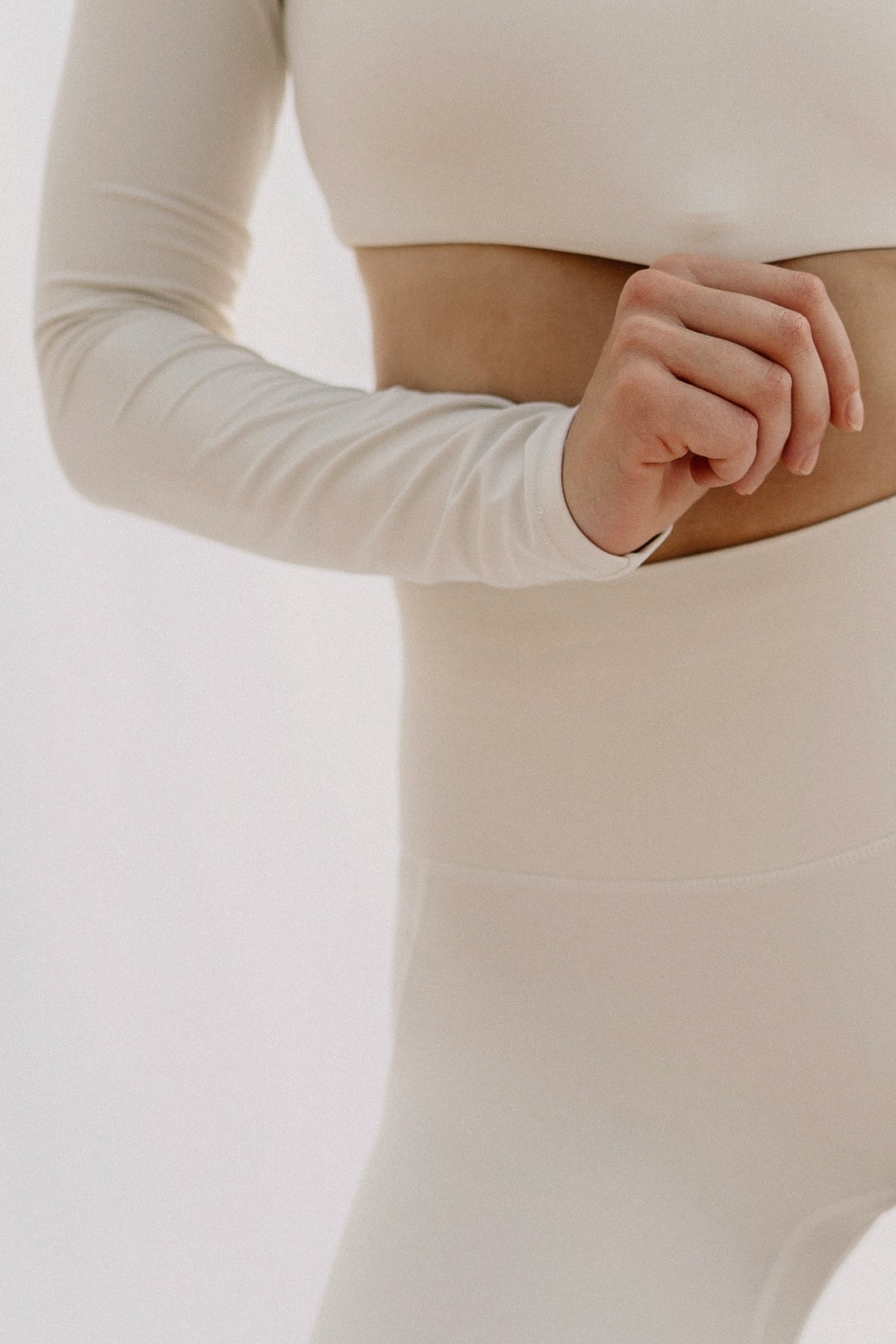 Person wearing a beige long-sleeve top and pants on a white background