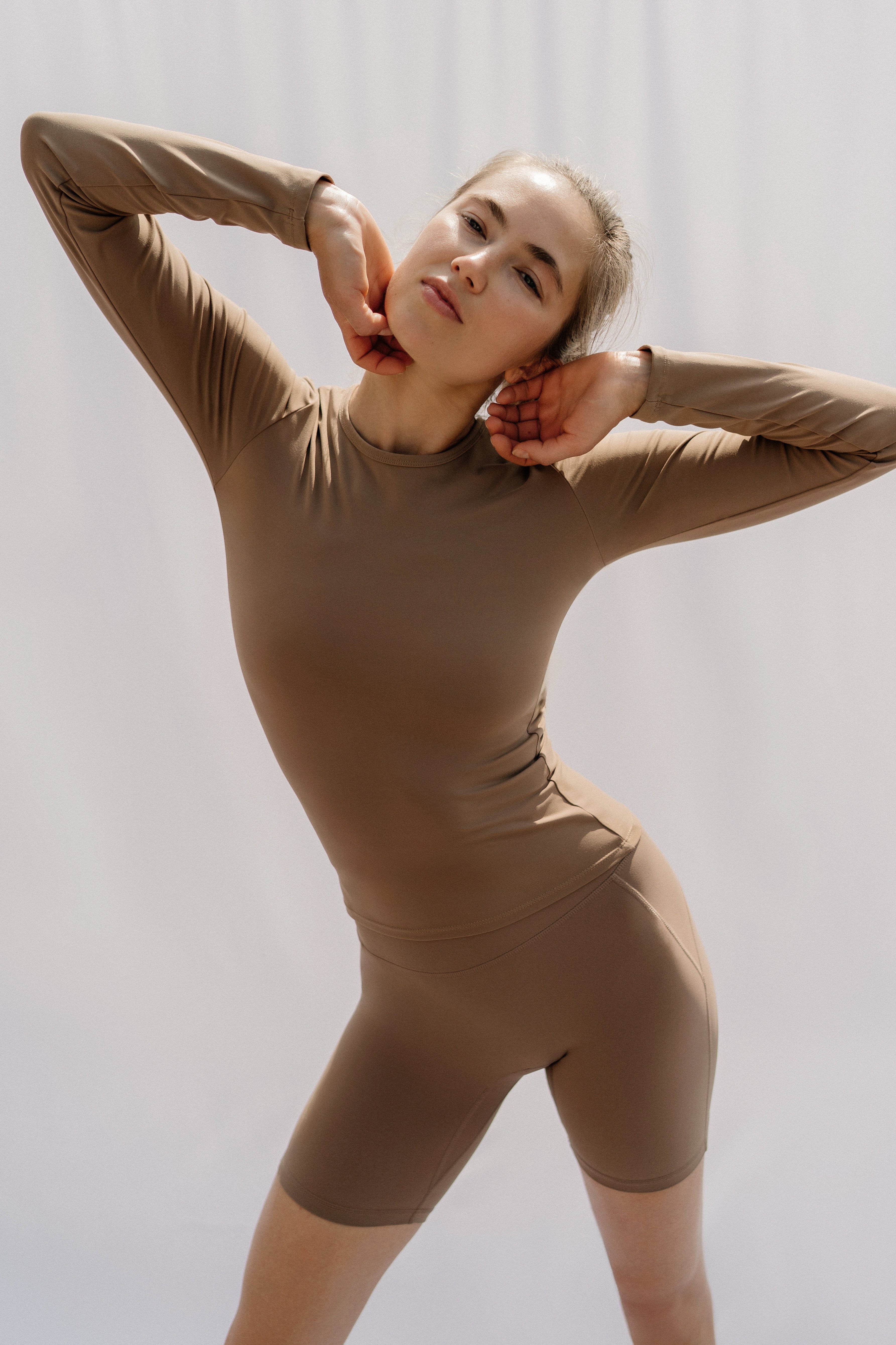 Woman wearing a brown long sleeve top and cycle shorts against a plain background