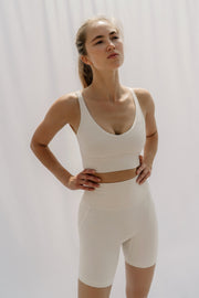 Woman wearing a white tank top and shorts against a plain background
