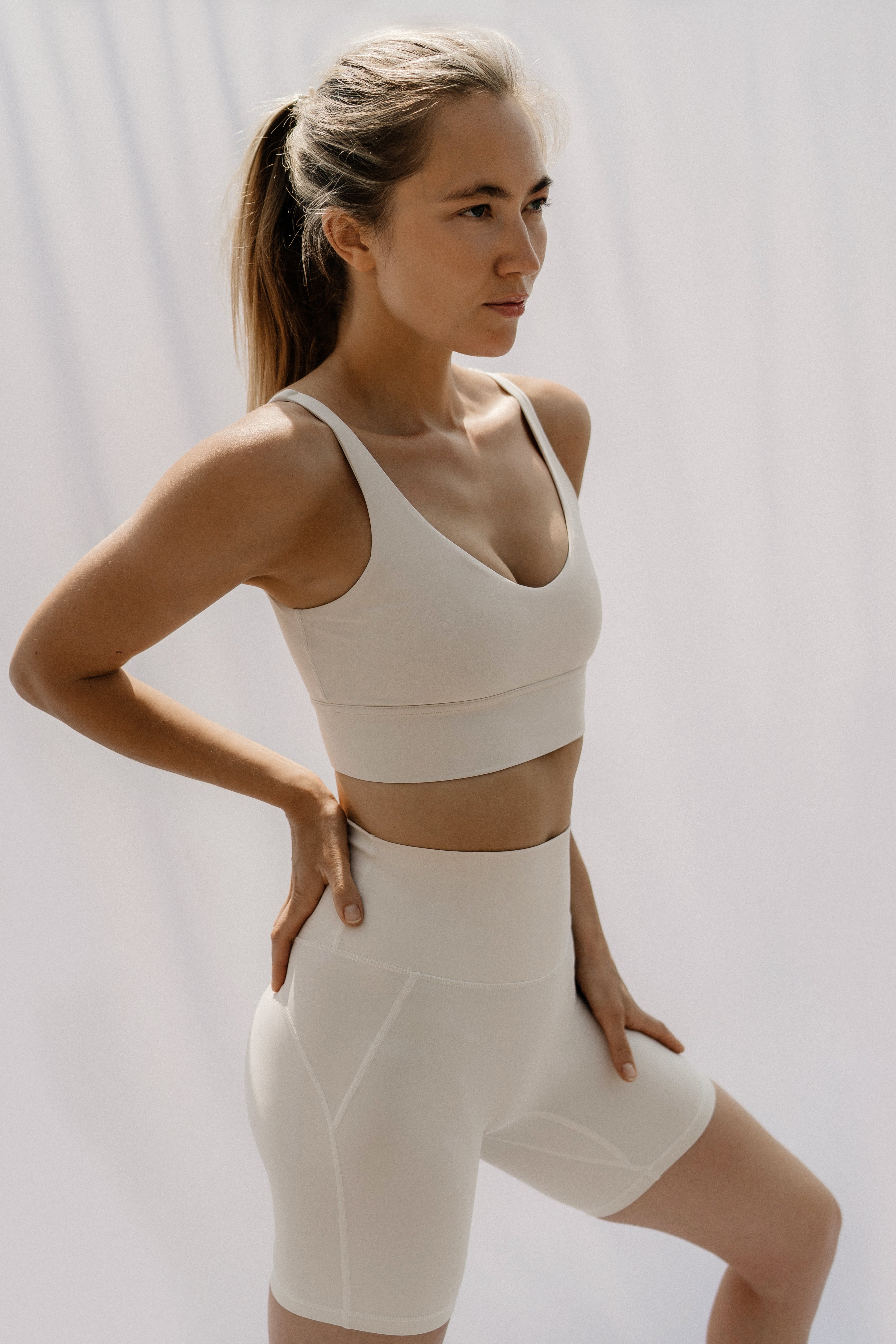 Woman wearing a white sports bra and shorts on a plain background