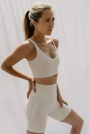 Woman wearing a white sports bra and shorts on a plain background