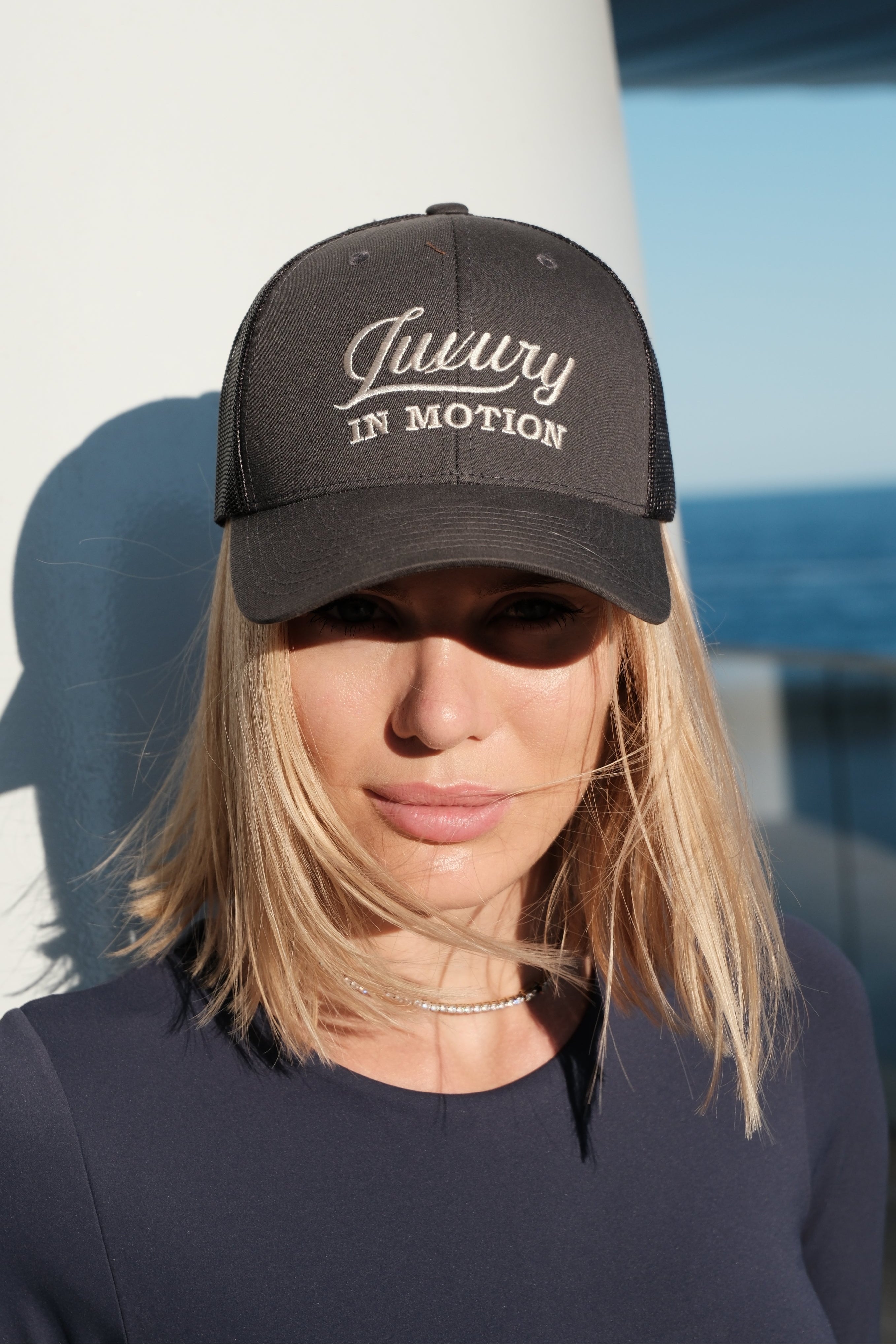 Person wearing a dark grey cap with 'Luxury in Motion' text against a light blue sky.