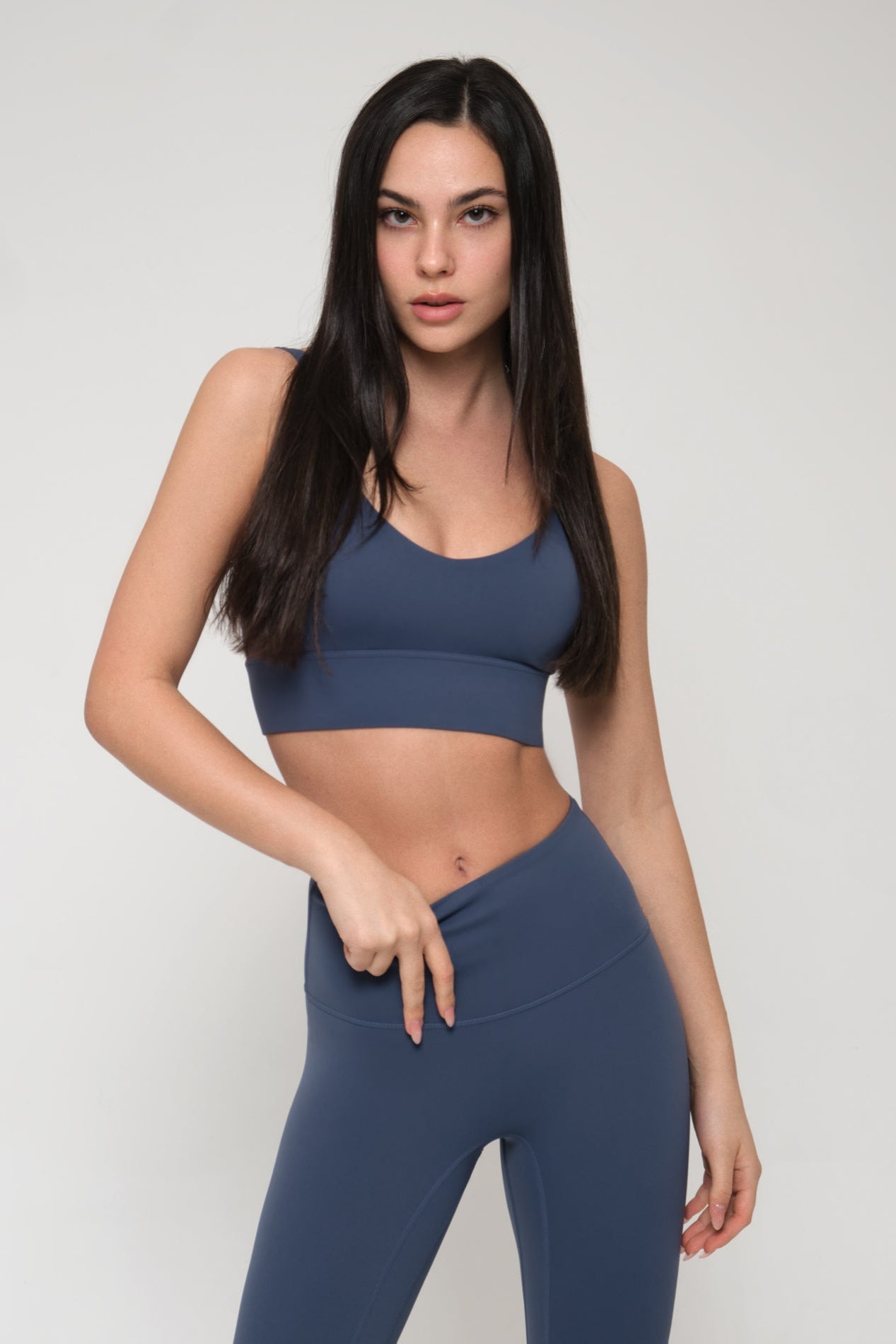 Woman wearing a blue sports bra and leggings on a light gray background