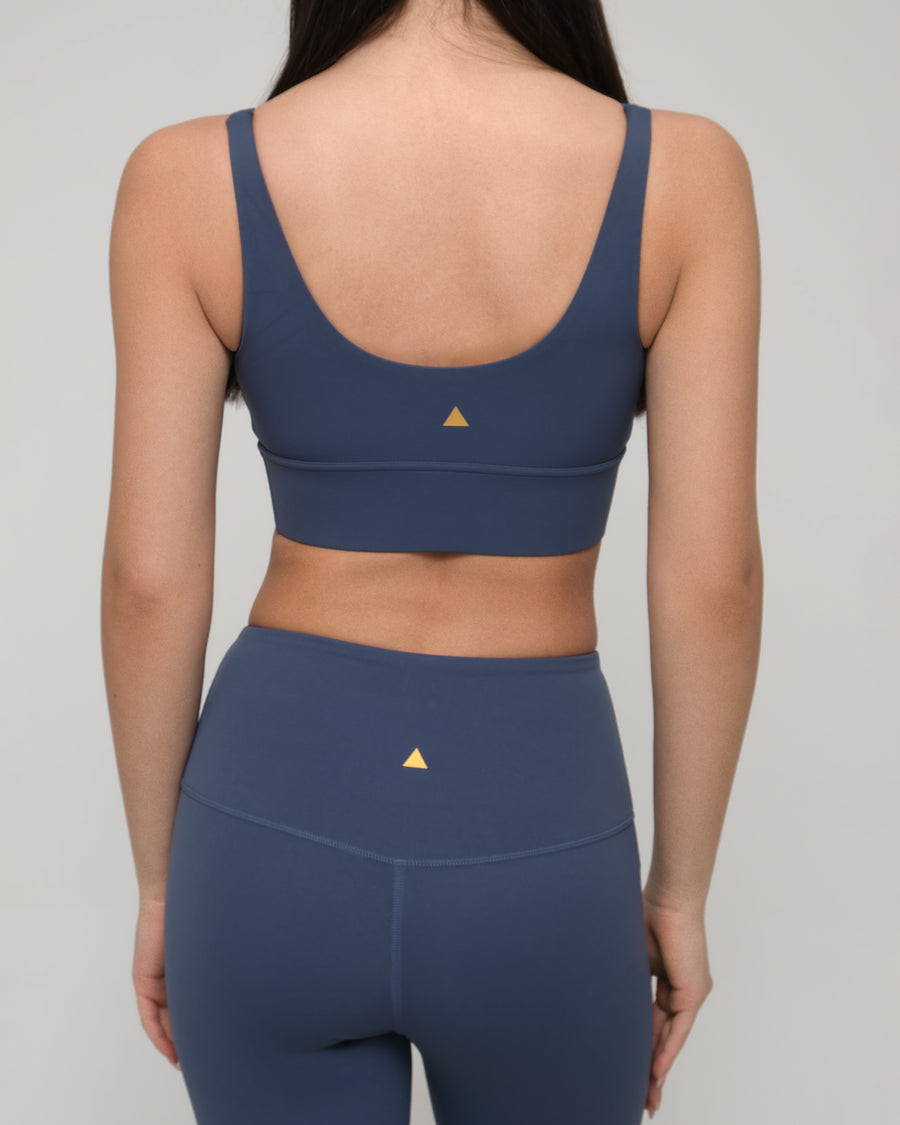 Woman wearing a blue sports bra and leggings set with a triangle logo on a plain background