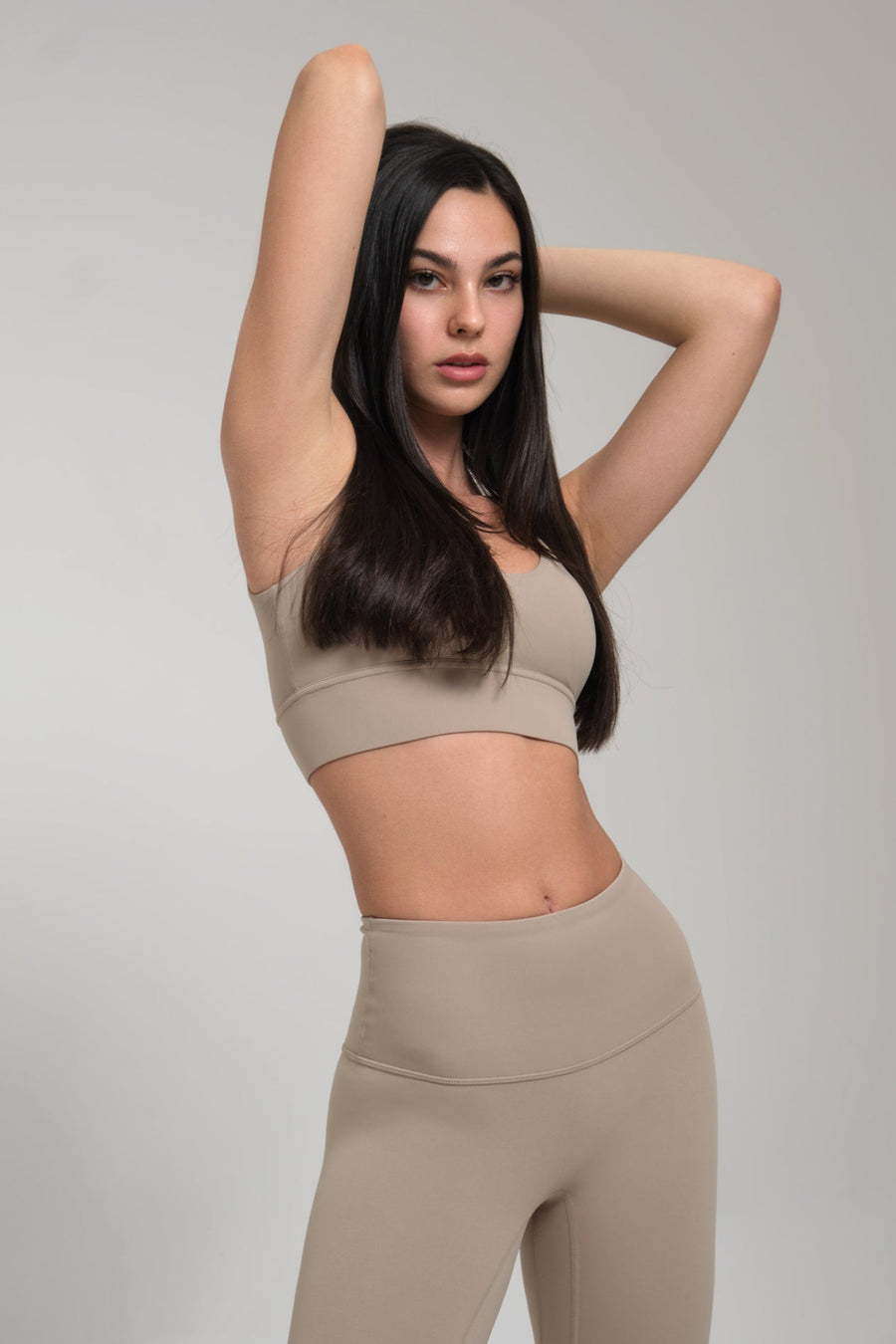 Woman wearing a beige sports bra and leggings against a gray background