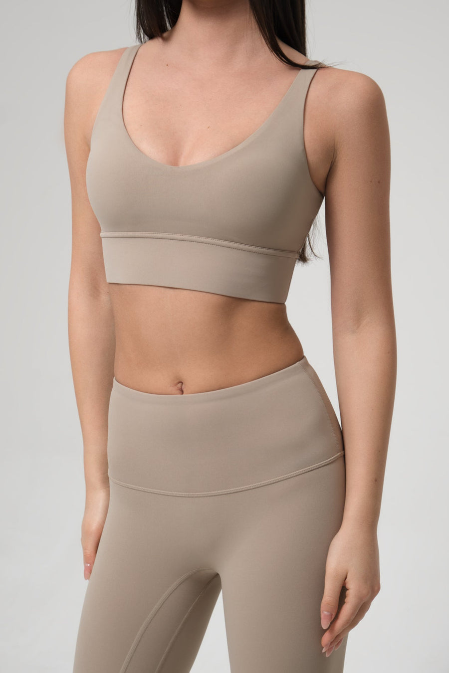 Woman wearing a beige sports bra and leggings set on a plain background
