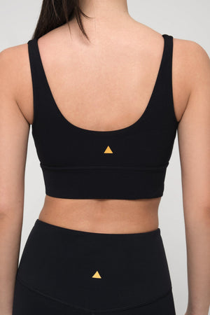 Black sports bra and leggings with a yellow triangle logo on a plain background