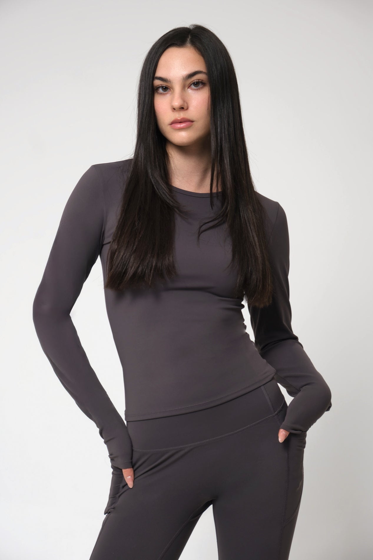 Woman wearing a dark gray long-sleeve top and leggings on a light gray background