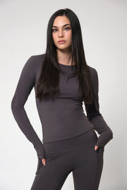 Woman wearing a dark gray long-sleeve top and leggings on a light gray background
