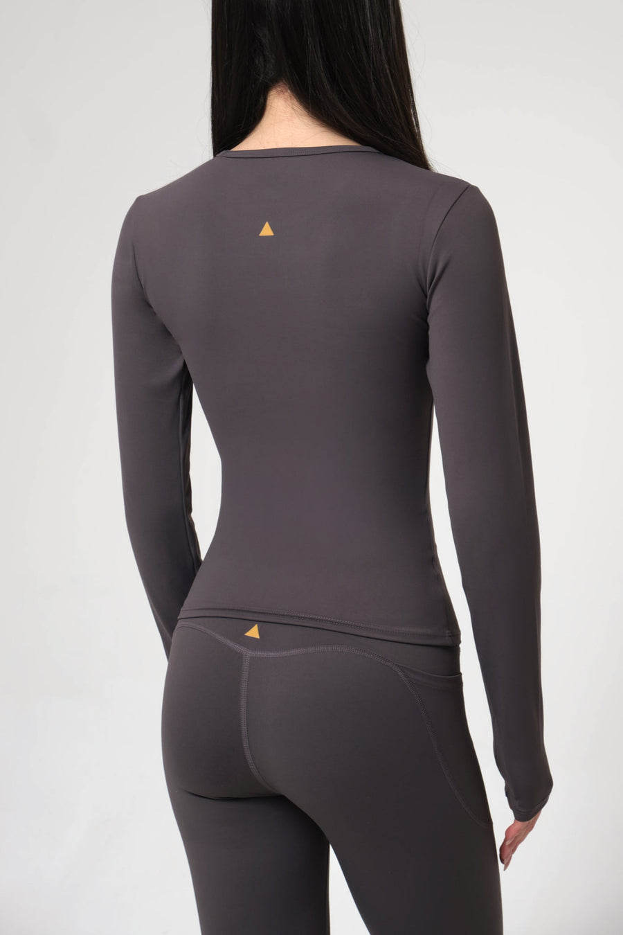 Woman wearing a gray long-sleeve athletic top and leggings on a light gray background