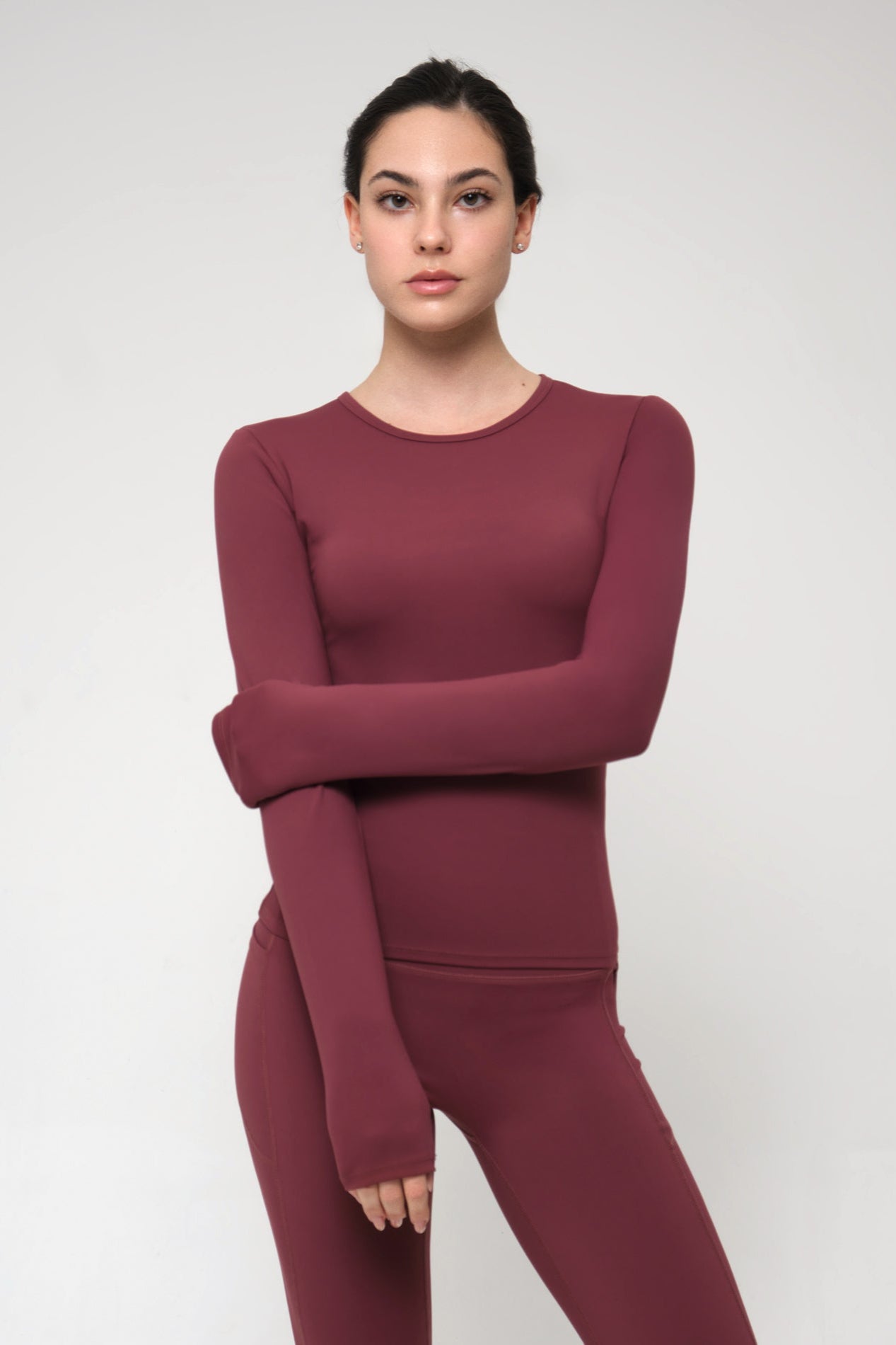 Woman wearing a burgundy long-sleeve top and leggings on a white background