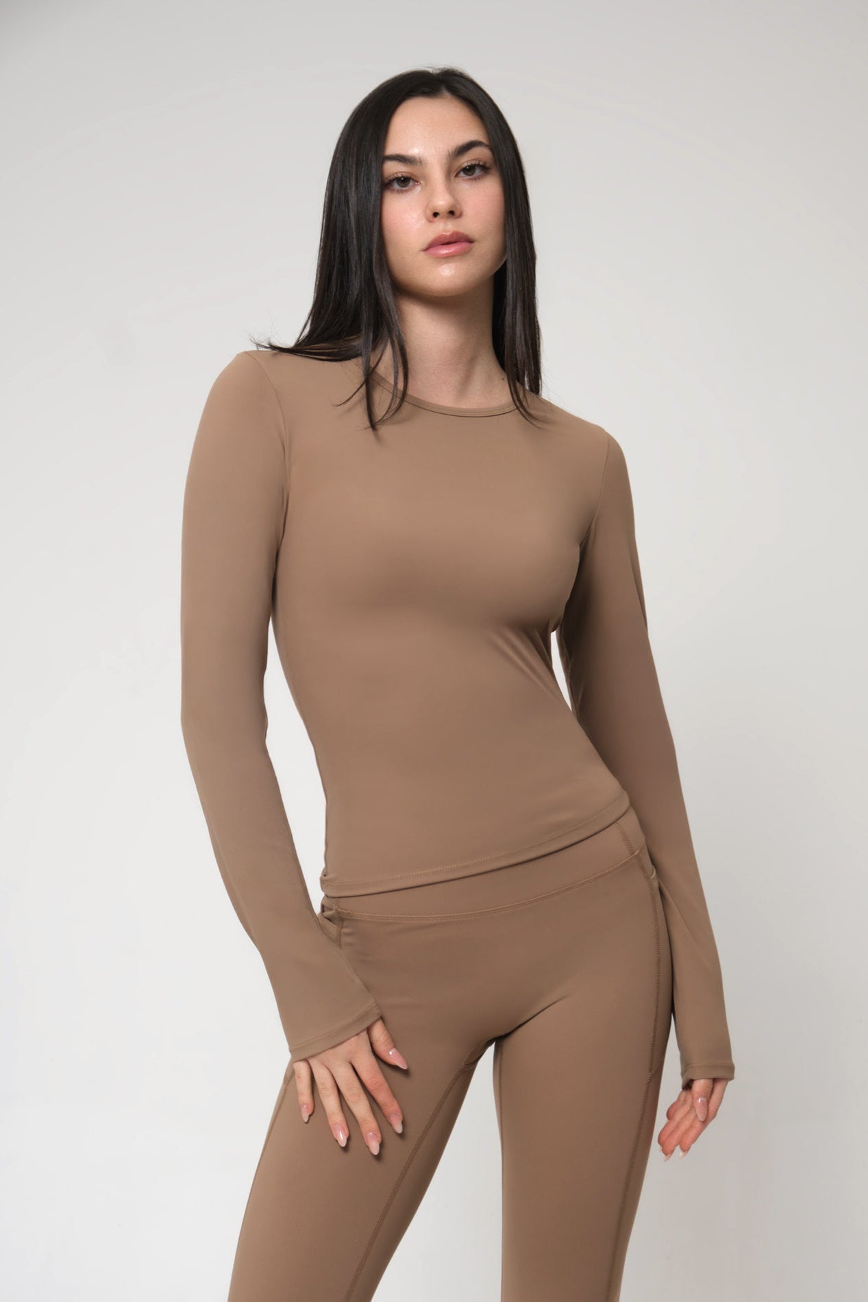 Woman wearing a brown long-sleeve top and leggings on a white background