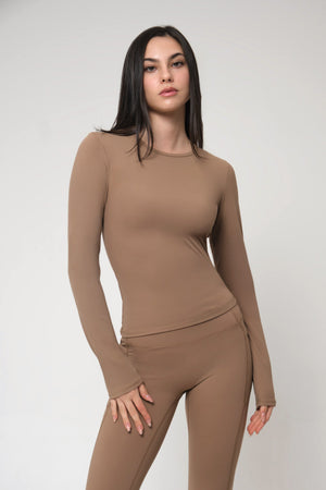Woman wearing a brown long-sleeve top and leggings on a white background