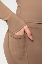 Brown long-sleeve top with a hand in the pocket on a light gray background